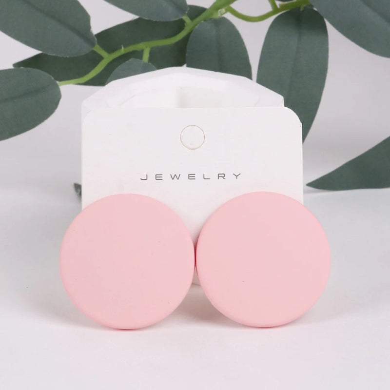 Pink earrings on a jewelry card with green leaves in the background