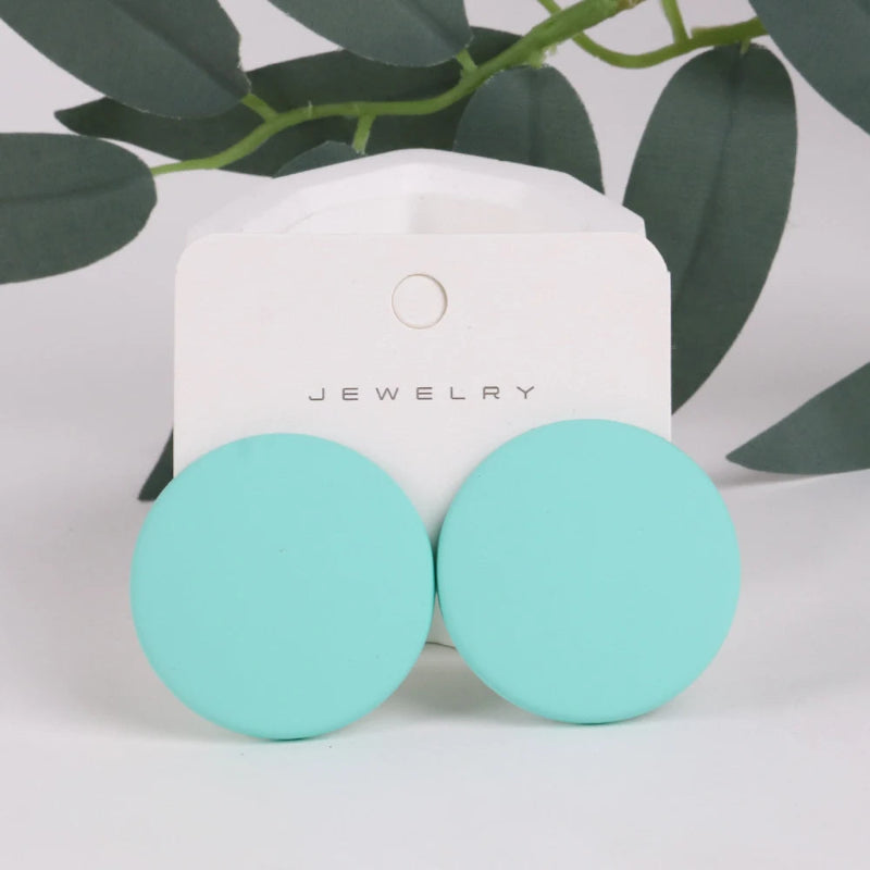 Turquoise earrings on a jewelry card with green leaves in the background