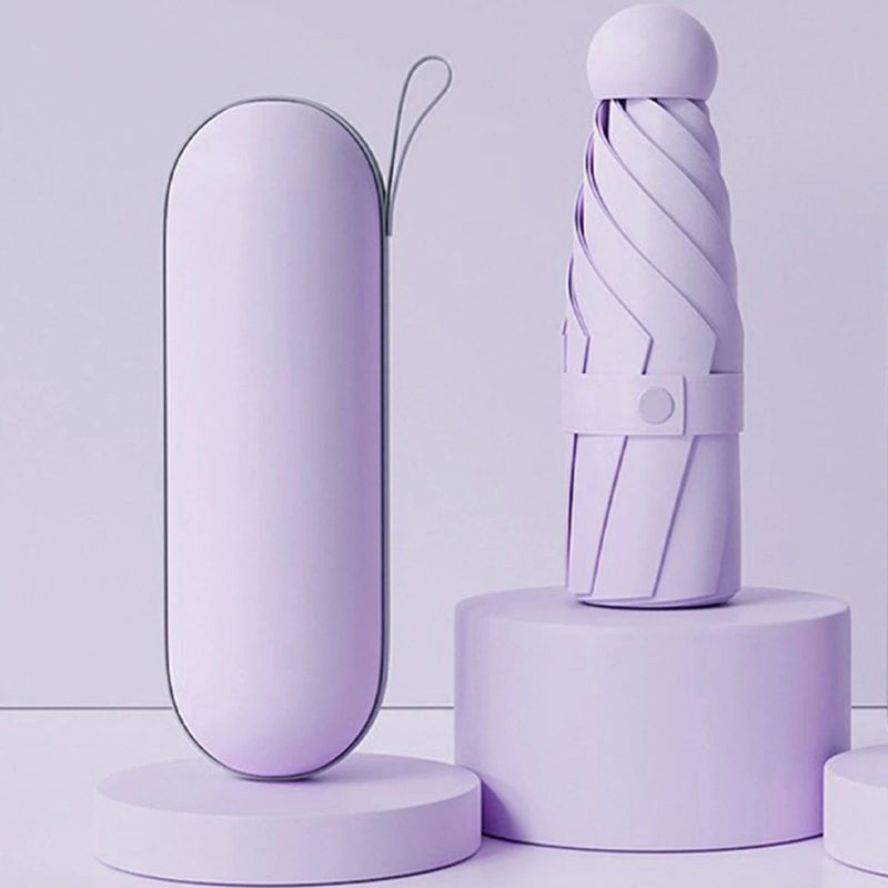A compact umbrella and its matching cylindrical case in a soft lavender color, displayed on minimalist round pedestals against a matching light lavender studio background.