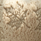 Close-up of a fluffy cream faux fur throw blanket featuring a detailed embroidered leaf pattern.