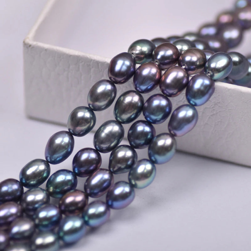 Close-up of a strand of iridescent baroque freshwater pearls draped over a white textured box on a light gray surface.