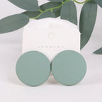 Pair of green round earrings on a white jewelry card with green leaves in the background.