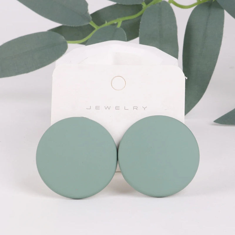 Pair of green round earrings on a white jewelry card with green leaves in the background.