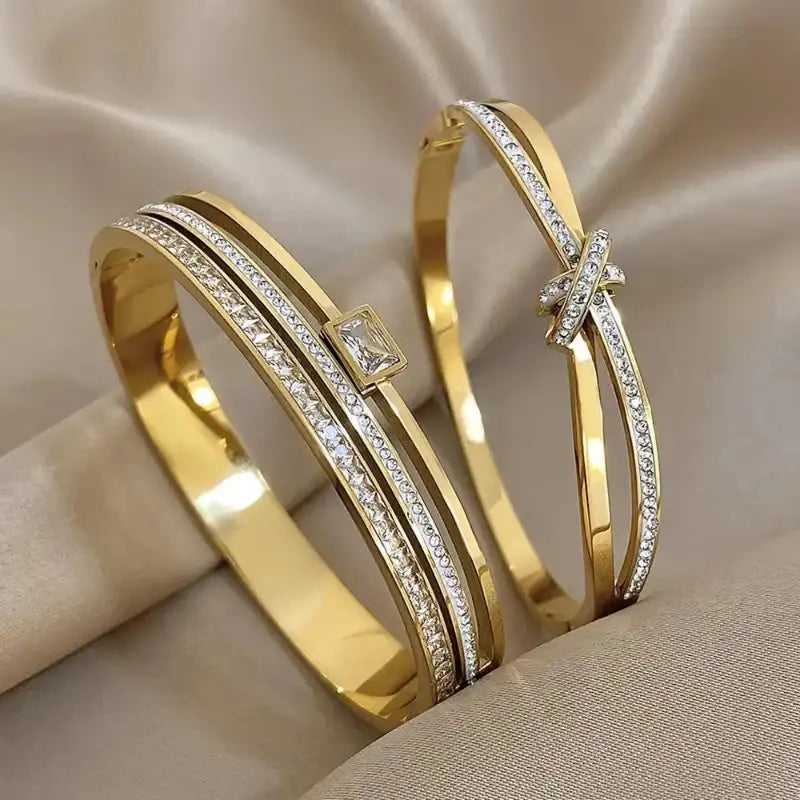 Two gold bangles with diamond accents on a beige fabric background