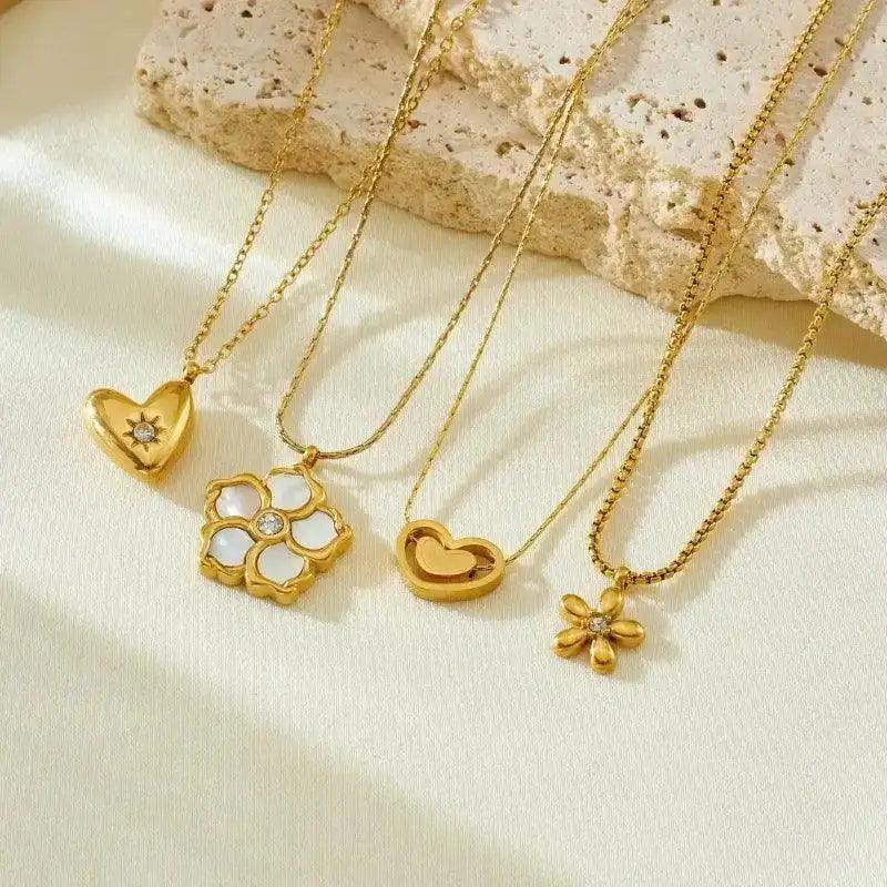 Gold necklaces with heart and flower pendants on a textured beige surface