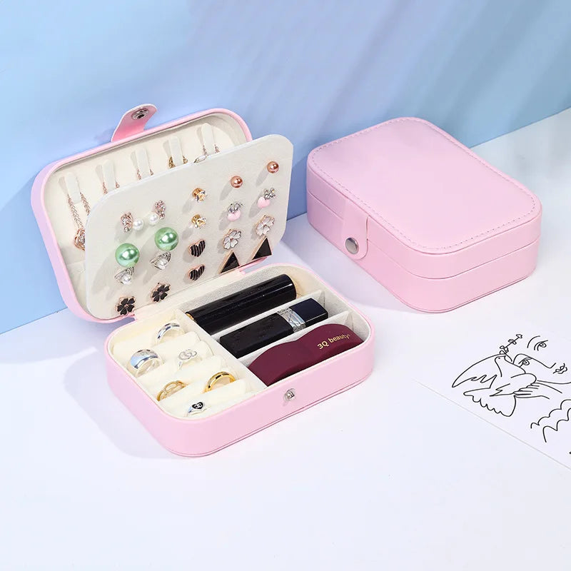 Pink jewelry box with compartments for earrings, rings, and lipsticks on a light blue background.