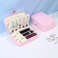 Pink jewelry box with compartments for earrings, rings, and lipsticks on a light blue background.