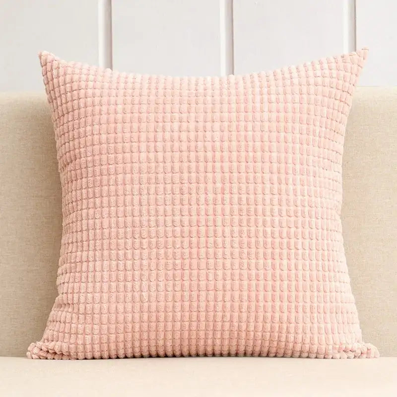 Pink textured pillow on a beige couch with a light gray wall background