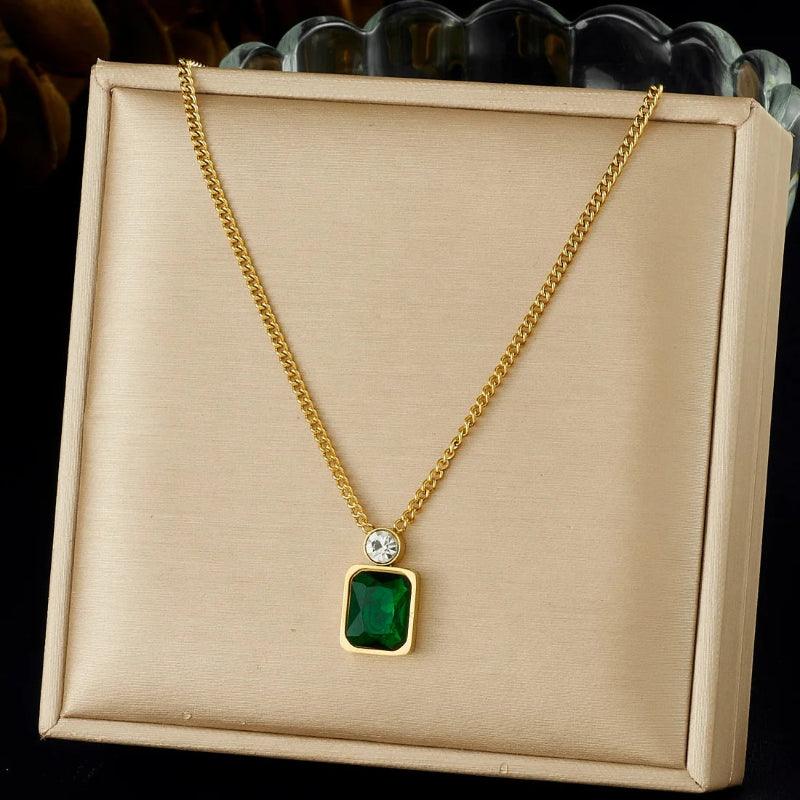 Gold necklace with a green pendant on a beige display box.