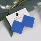Blue square earrings on a jewelry card with green leaves in the background