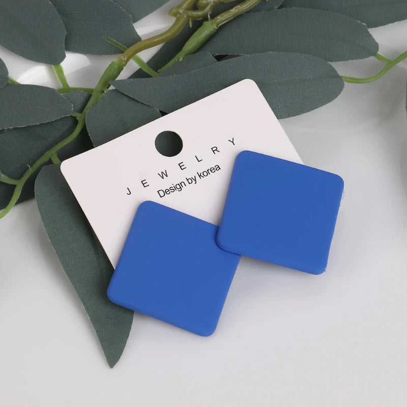 Blue square earrings on a jewelry card with green leaves in the background