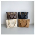 Four patterned handbags with gold chains on a black surface against a light gray wall.