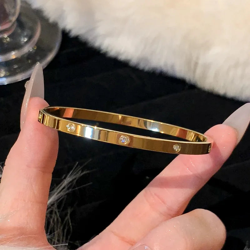 Gold bracelet with diamonds held by a hand against a blurred background