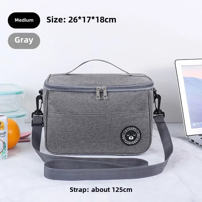 Gray insulated lunch bag with strap on a white surface, surrounded by snacks and a laptop.