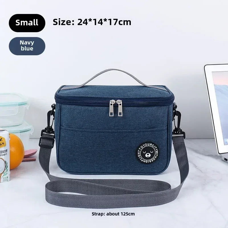 Navy blue cooler bag with strap on a white surface, surrounded by items like a laptop and snack.