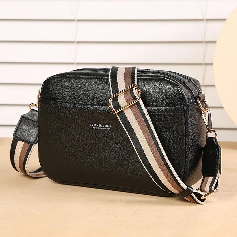 Black leather bag with a striped strap on a beige surface