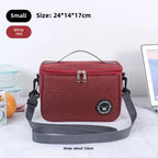 Red cooler bag with gray strap on a white surface, surrounded by items like a laptop and fruit.