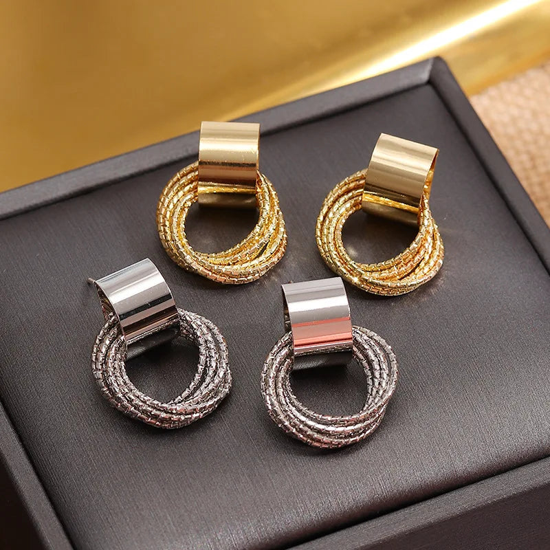 Pair of earrings with gold, silver, and rose gold finishes on a dark surface.