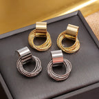 Pair of earrings with gold, silver, and rose gold finishes on a dark surface.