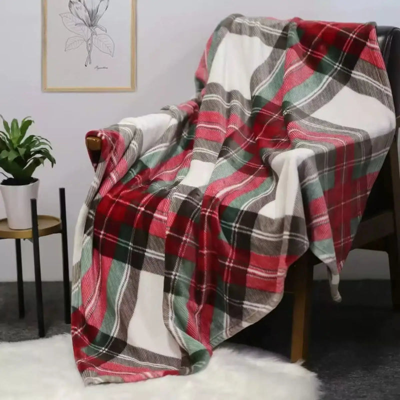 A plaid throw blanket draped over a wooden chair in a styled room setting, featuring a pattern of red, green, black, and white.