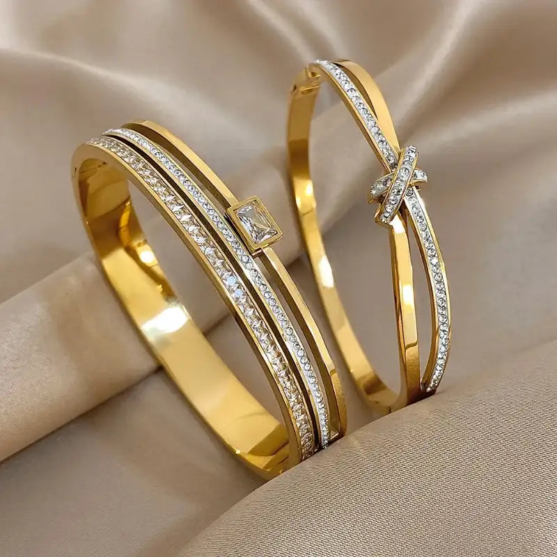 Two gold bracelets with diamond accents on a beige fabric background