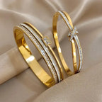 Two gold bracelets with diamond accents on a beige fabric background