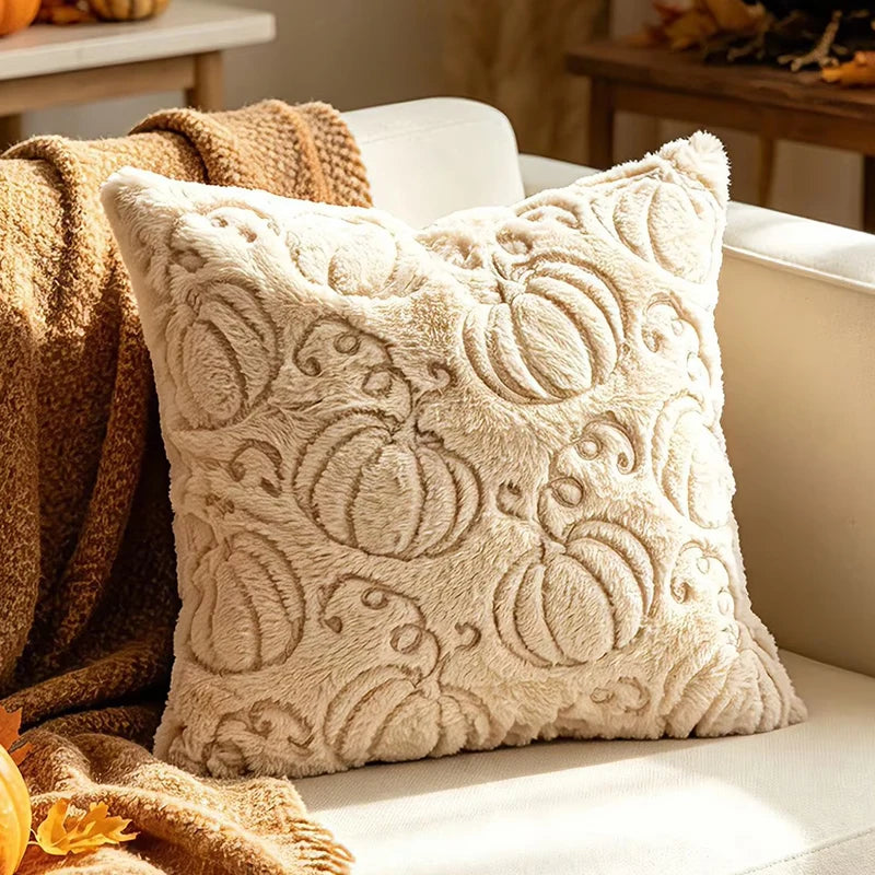 A square cream throw pillow with a raised pumpkin pattern, styled on a white sofa next to a brown knit blanket.