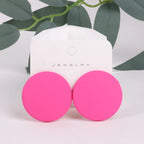 Pink earrings on a jewelry display card with green leaves in the background