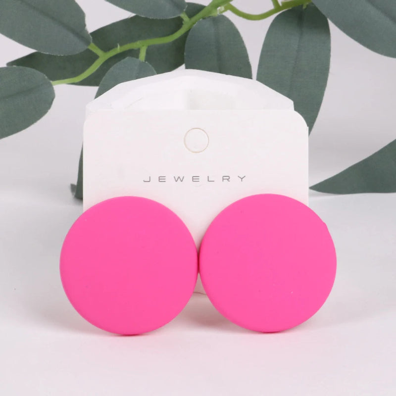 Pink earrings on a jewelry display card with green leaves in the background