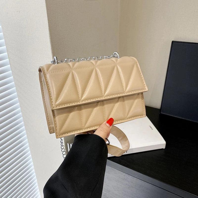 Beige quilted handbag held by a person with red nail polish, against a neutral background.