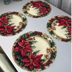 Four round holiday table placemats with a Christmas poinsettia and holly pattern, arranged on a white tabletop.