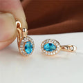 Gold earrings with blue gemstones held by a hand on a white surface.