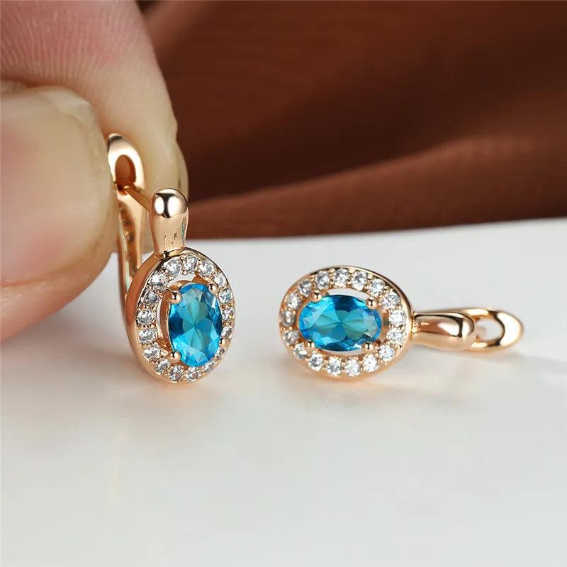 Gold earrings with blue gemstones held by a hand on a white surface.