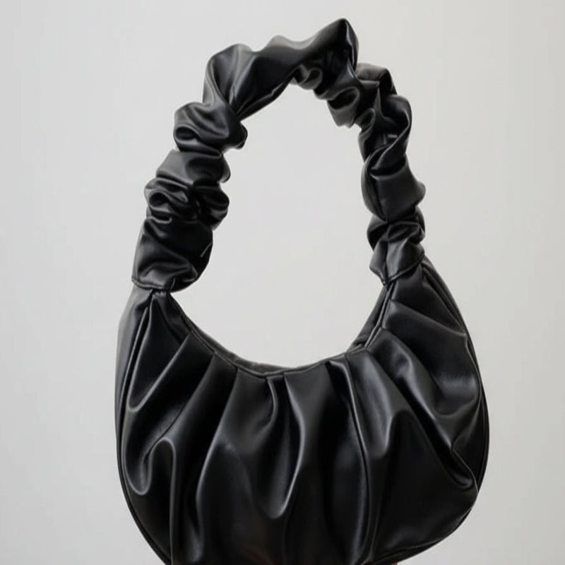 Black ruched handbag held by a hand on a neutral background