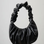 Black ruched handbag held by a hand on a neutral background