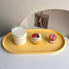 Yellow tray with a glass of milk, a dessert, and a small jar on a white surface.