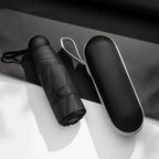 Black umbrella and its case on a white surface with a dark background