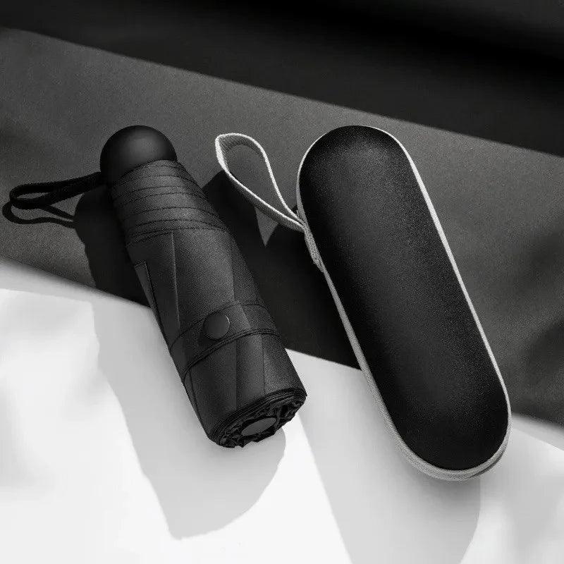 Black umbrella and its case on a white surface with a dark background