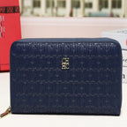 A navy blue zip-around wallet with an embossed monogram pattern and a small gold logo on the front, displayed on a white surface with a blurred city street background.