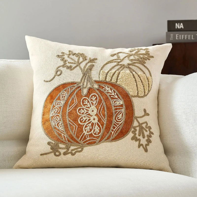 Decorative pillow with embroidered pumpkins on a beige couch.