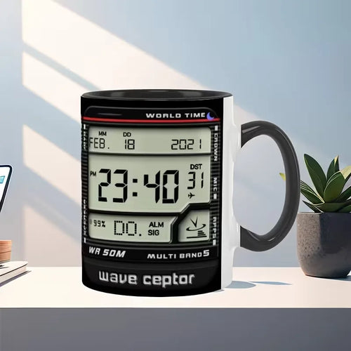 A black ceramic mug with a digital alarm clock face design printed on it, shown on a white desk with a plant and laptop in a styled indoor setting.