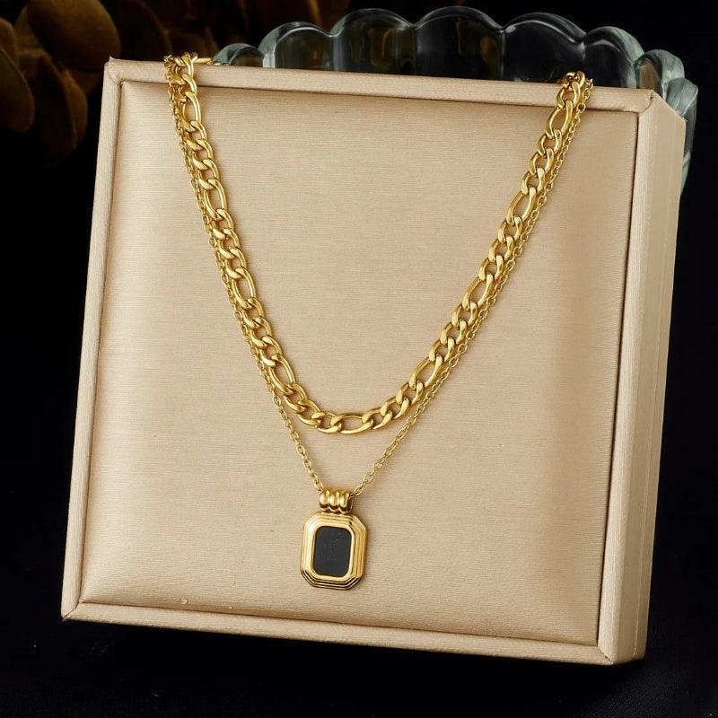 Gold chain necklace with a pendant on a beige display box against a dark background