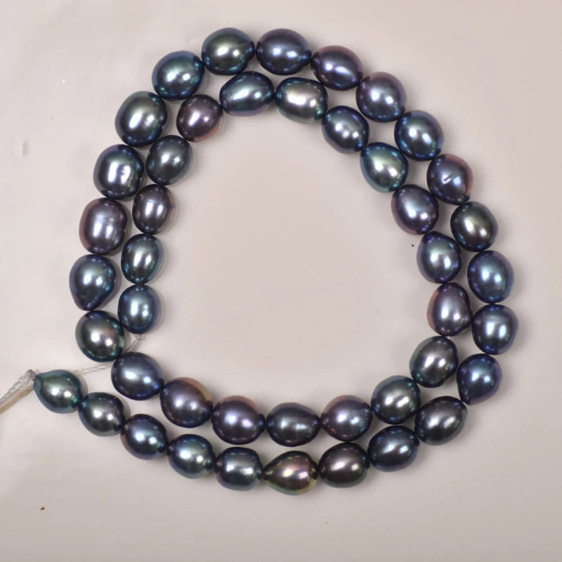 A strand of irregular baroque freshwater pearls arranged in a loop on a plain light background. The pearls have a deep blue-green iridescent sheen with subtle purplish undertones.
