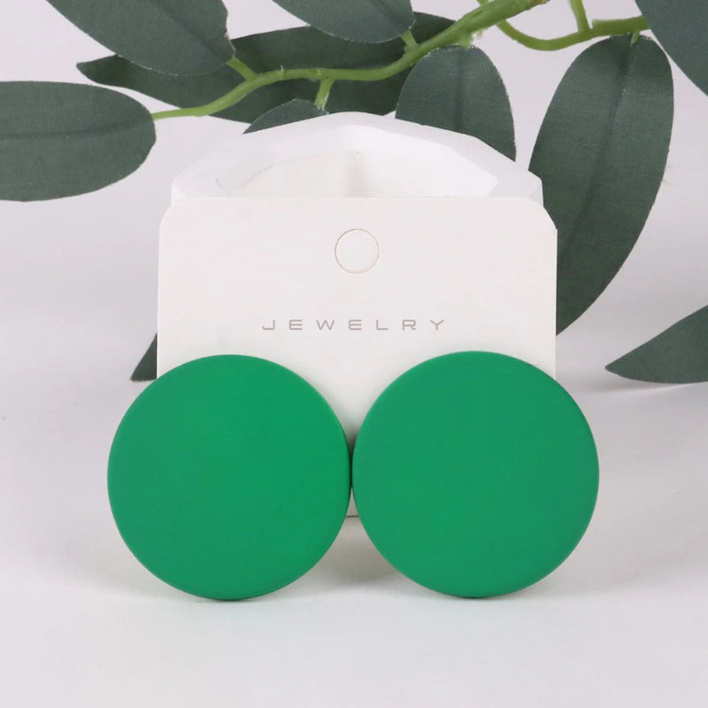 Green round earrings on a white jewelry card with green leaves in the background