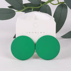 Green round earrings on a white jewelry card with green leaves in the background