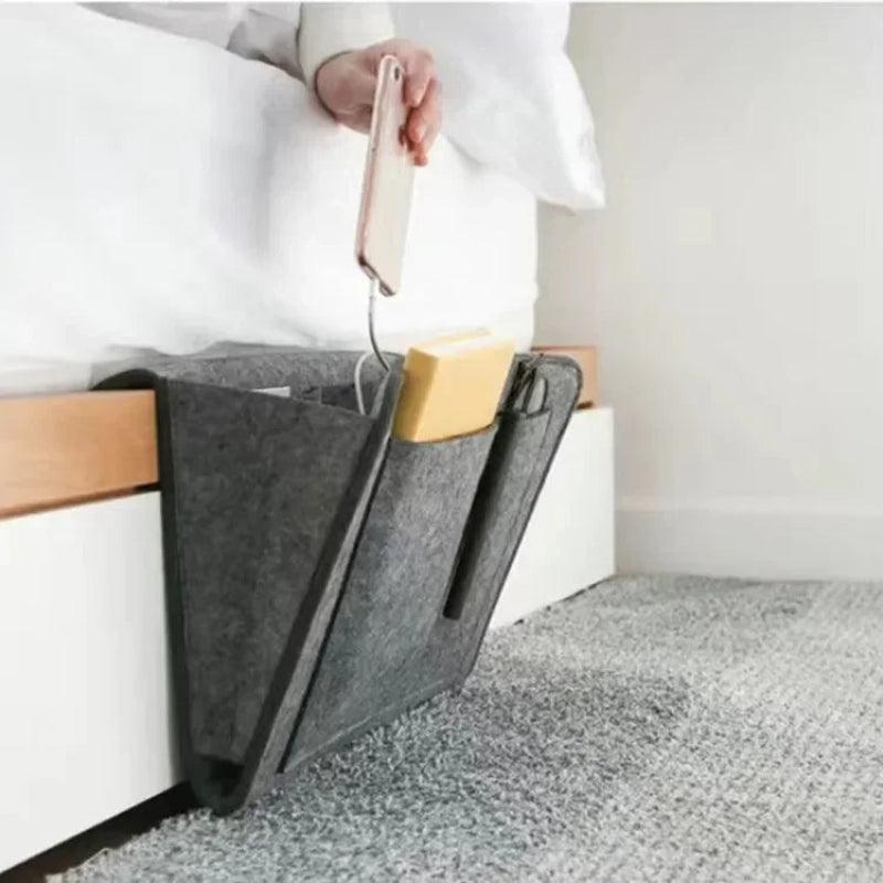 Gray felt bedside caddy with books and a phone on a bed.