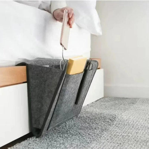 Gray felt bedside caddy with books and a phone on a bed.