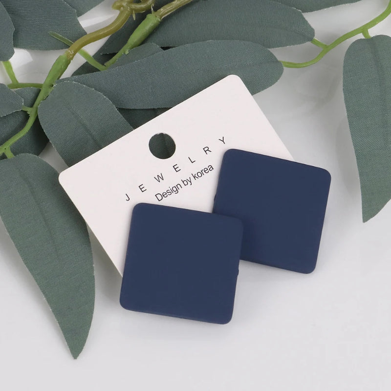 Navy blue square earrings on a white jewelry card with green leaves in the background