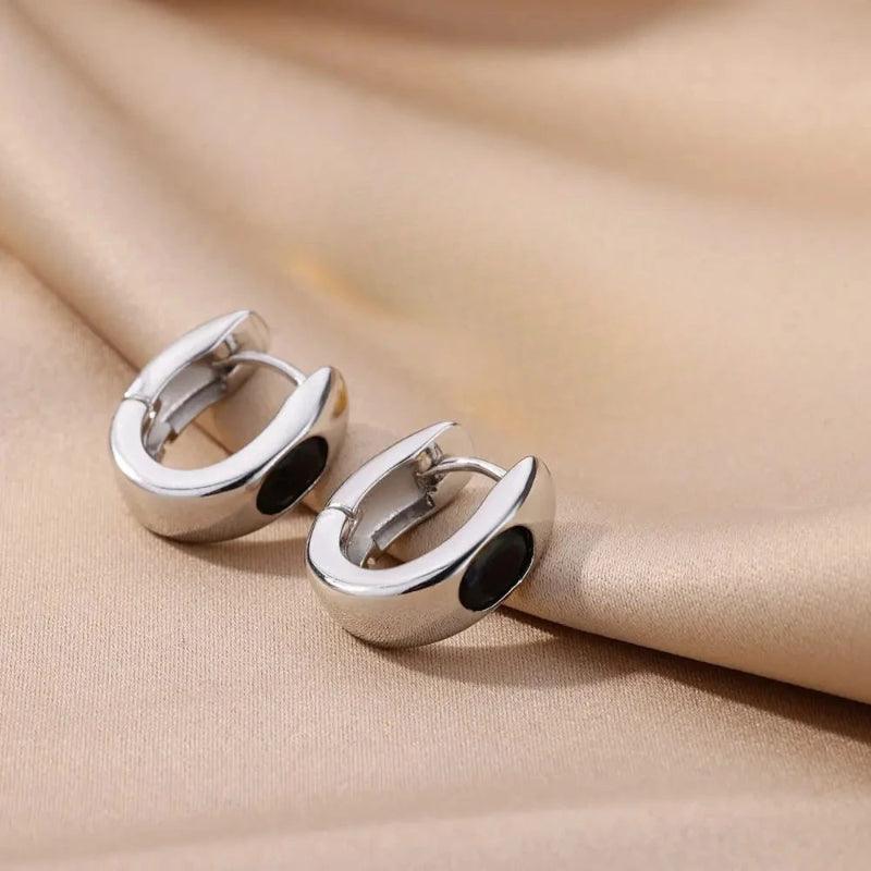 Pair of silver hoop earrings with black centers on a beige fabric background