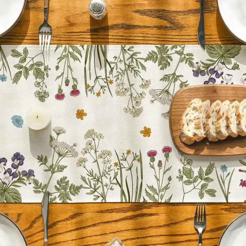 Table setting with floral placemat, bread, and candles on a wooden table.